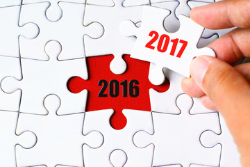 "2016" word on missing puzzle with a hand hold a piece of "2017" word puzzle want to complete it - business and finance concept