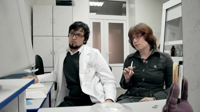 Scientific Laboratory / Research Team / Monitoring Room. Two young scientists, a man and a woman, sitting in the lab looking computer CRT monitor.