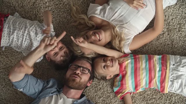 Top view of parents and their little kids lying on the floor at home and playing, touching their fingers and laughing cheerfully 
