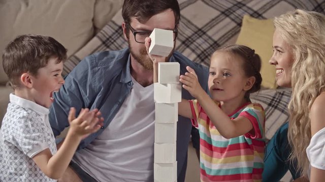 Parents and their little kids enjoying game with toy bricks, trying to make a tower higher but ruining it in the end  