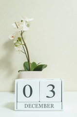 Closeup white wooden calendar with black 3 december word with white orchid flower on white wood desk and cream color wallpaper in room textured background , selective focus at the calendar
