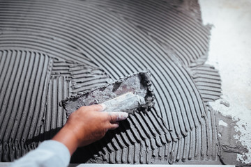 close up of worker hand plastering a wall, adding adhesive with comb trowel