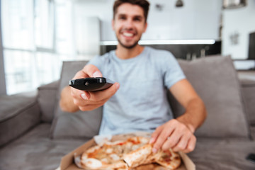 Man pushing button on remote control while holding pizza