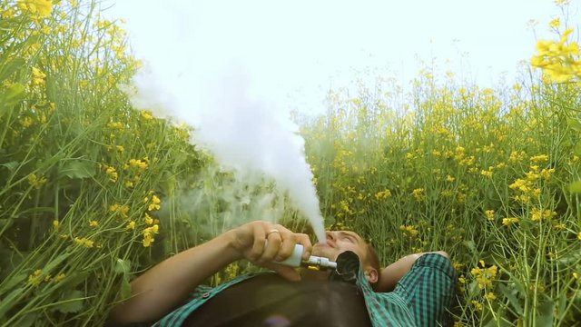 young man is vaping in yellow field, man lying in a yellow field