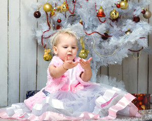 Little child sits near new year tree with gift box