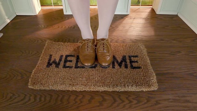 Legs of woman stepping on welcome mat