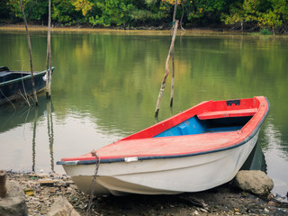 Picture of the landscape scene in the forest. With fishing boat on the near river-bank and depths of a green forest on the far bank. Boat with red top laying on the stony shore of the river.