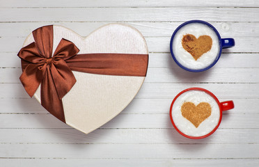 Two cups of coffee with heart shape symbol and gift box on woode