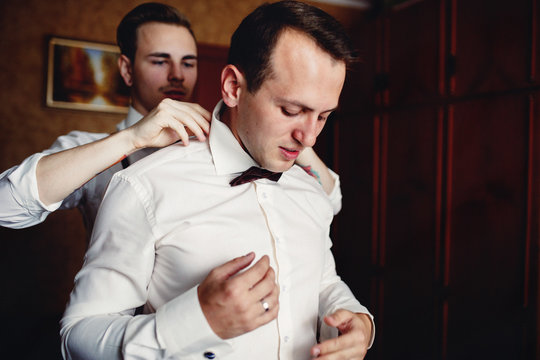 Best man is helping to the groom with collar