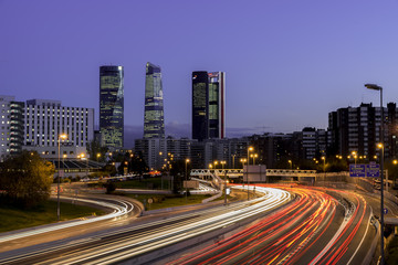 Obraz na płótnie Canvas Atardecer de Madrid con los rascacielos y las luces de la carretera
