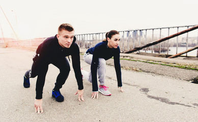 Couple athletes are at a low start on city bridge