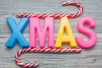 Bunte Plastikbuchstaben XMAS mit Zuckerstangen auf grauem Holz Hintergrund