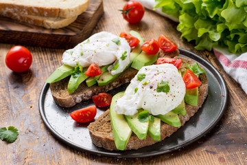 Close up view of delicious poached egg and avocado toasts garnished with chopped parsley. Selective focus