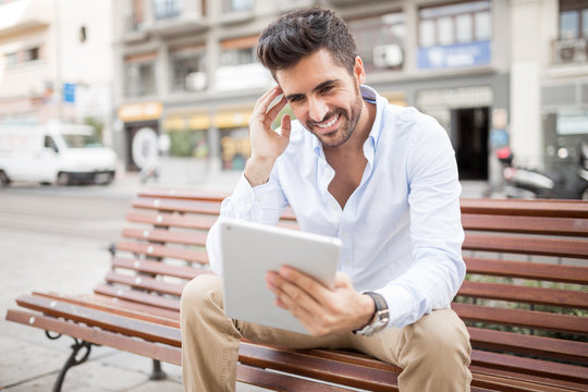 Young man using digital tablet while sitting on bench outdoors