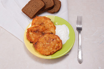 Potato pancakes with meat and sour cream on green plate with rye
