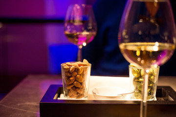 Amazing Close Up View of Two Glasses of White Wine and Cups of Nuts in the Luxury Bar with Blurred Magenta Background, Horizontal View