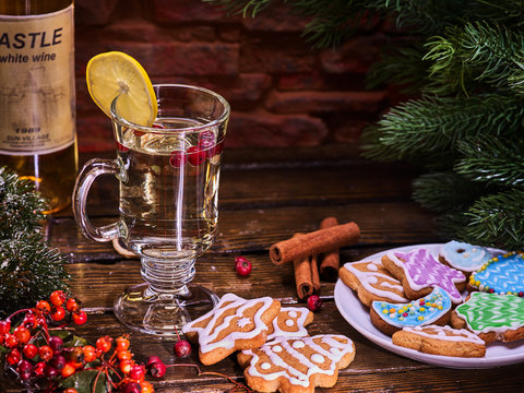 Christmas cookies on plate with fir branches. Christmas still life with mug decoration lemon slice hot drink on wooden table. Brick wall background.