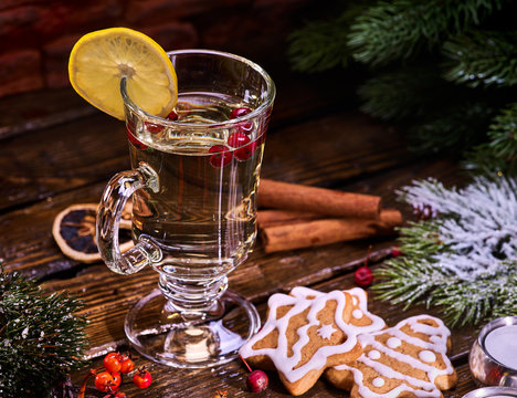 Christmas glass latte mug and Christmas star form cookies on plate with fir branches. Mug decoration lemon slice on wooden table in restaurant and cinnamon sticks.