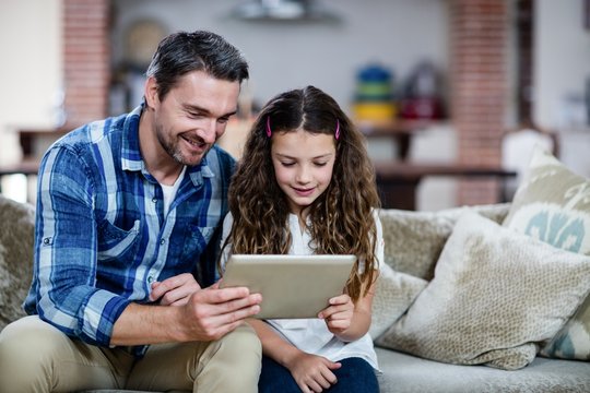 Father and daughter using digital tablet in living room