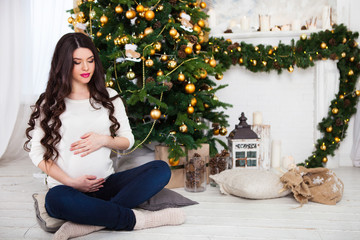 Happy young pregnant woman sitting near the Christmas tree