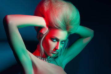 Studio beauty photo of blonde girl with creative make-up and hairstyle with colored lights on a light background