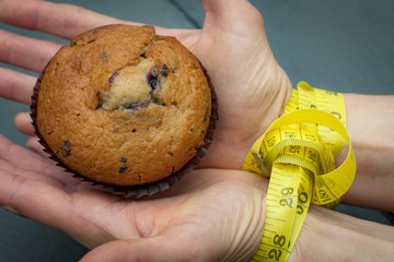 Diet, bondage and delayed gratification concept with woman hand reaching for a muffin while her hands are tied together with measuring tape a symbol of dieting and self control. - obrazy, fototapety, plakaty