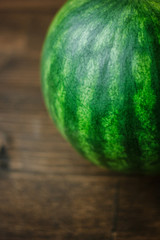 Close-up view of whole undivided watermelon. Green fresh watermelon on brown wooden background.