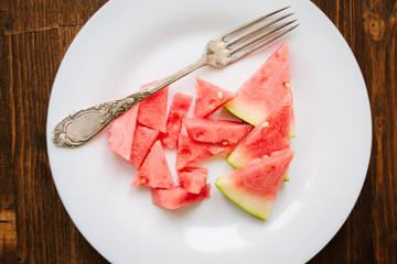 Small pieces of ripe watermelon and fork on the white plate over wooden background