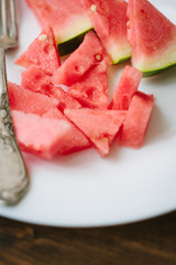 Small pieces of ripe watermelon and fork on the white plate over wooden background