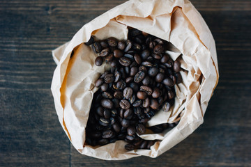 Coffee beans - roasted seeds of coffee in paper bag over the wood board