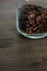 Transparent glass coffee jar filled with beans of coffee over the dark wooden table.