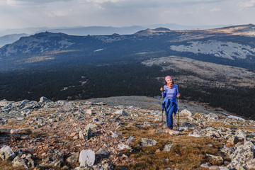 Happy young woman traveler climbs the mountain with trekking pole. Healthy and sport lifestyle concept.