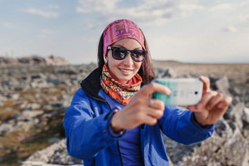 Cute woman traveler in mountain hike photographed selfie on a smartphone