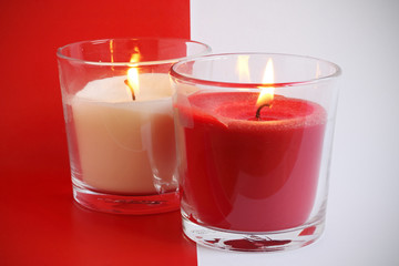 Dos velas encendidas, roja y blanca, sobre fondo blanco y rojo