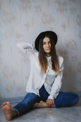 Beauty girl sitting on the floor in black hat, white shirt and blue jeans 