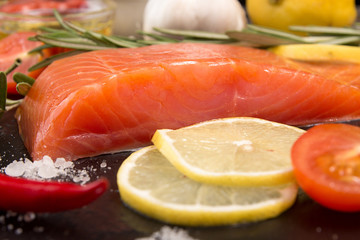 Salmon fillet, chili pepper, lemon slice and tomato over on blac