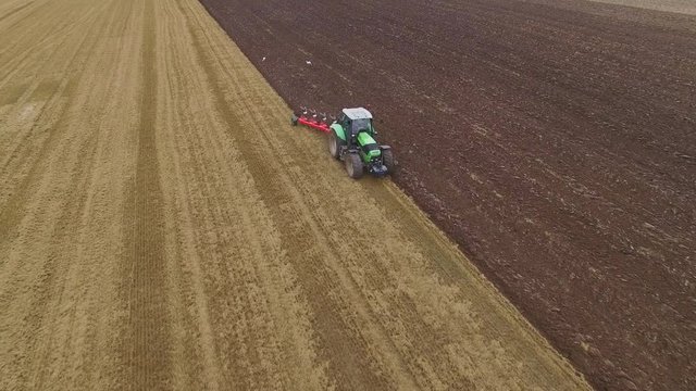 Aerial Shot of a Tractor Plowing Field. Clear Line of Completed Work is Visible.