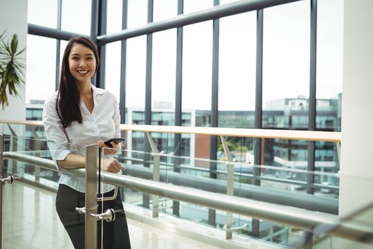 Smiling businesswoman holding mobile phone in office corridor