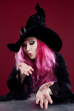 Attractive woman in witches hat and costume with red hair blows away something with hands, place for your text or photo manipulation