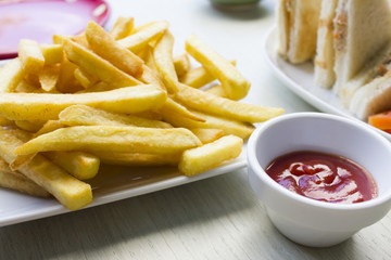 Tasty french fries in dish with tomato sauce on wooden table bac