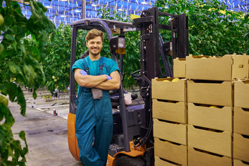 Young attractive man working on electric forklift in greenhouse