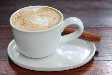 Hot cappuccino coffee in white cup with cinnamon stick.