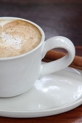 Hot cappuccino coffee in white cup with cinnamon stick.