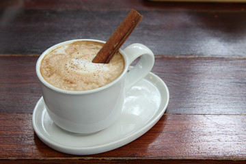 Hot cappuccino coffee in white cup with cinnamon stick.