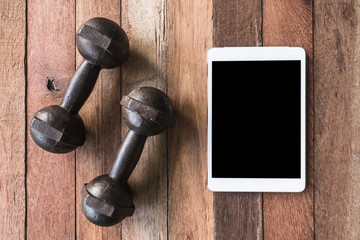 Top view of iron dumbbells with Tablet on wooden table background