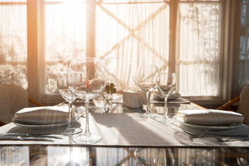 Glasses and plates on table. Dining table beside a window. Invite relatives for breakfast. Create perfect cleanliness.