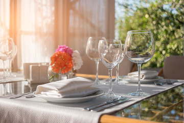 Plates and glasses on table. Dining table and sunshine. Invite neighbours for lunch. Create the perfect cleanliness.