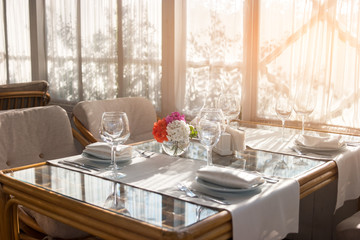 Table with plates and wineglasses. Table and chairs beside window. Invite your friends for breakfast. Cleanliness and perfect order.