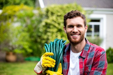 Smiling man carrying garden hose in backyard 