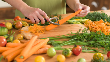 womans hands is slicing carrot on wooden board near vegetables